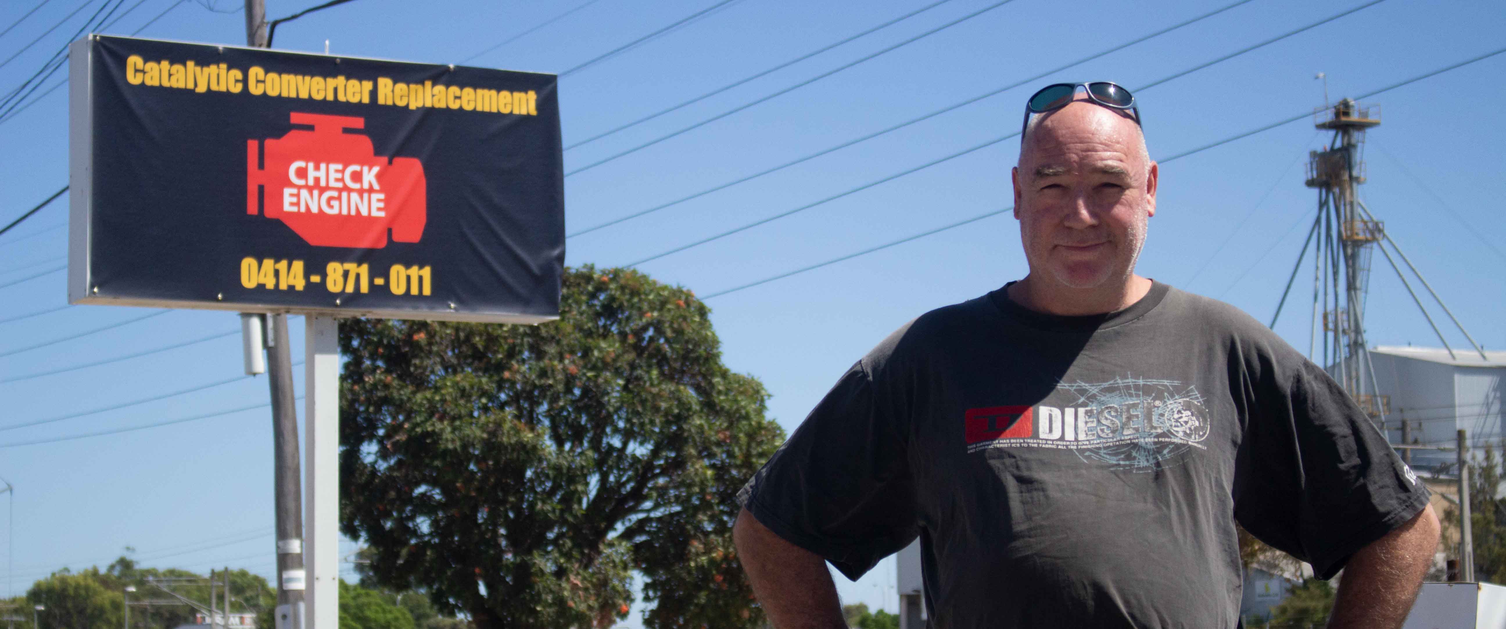 John Aretz standing in front of a Catalytic Converter Replacement sign